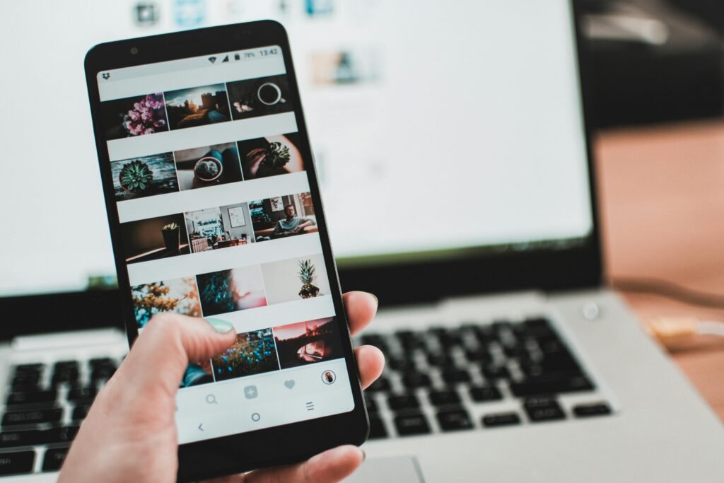 Hand holding a smartphone displaying a photo gallery in front of a laptop