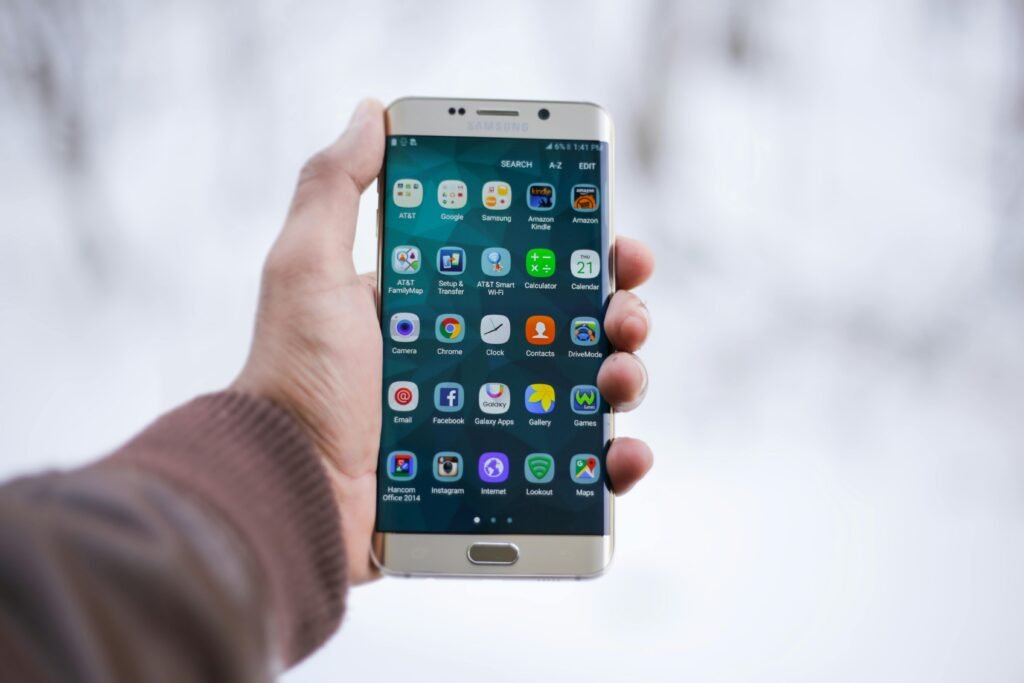 A hand holding a smartphone showing various app icons on the home screen