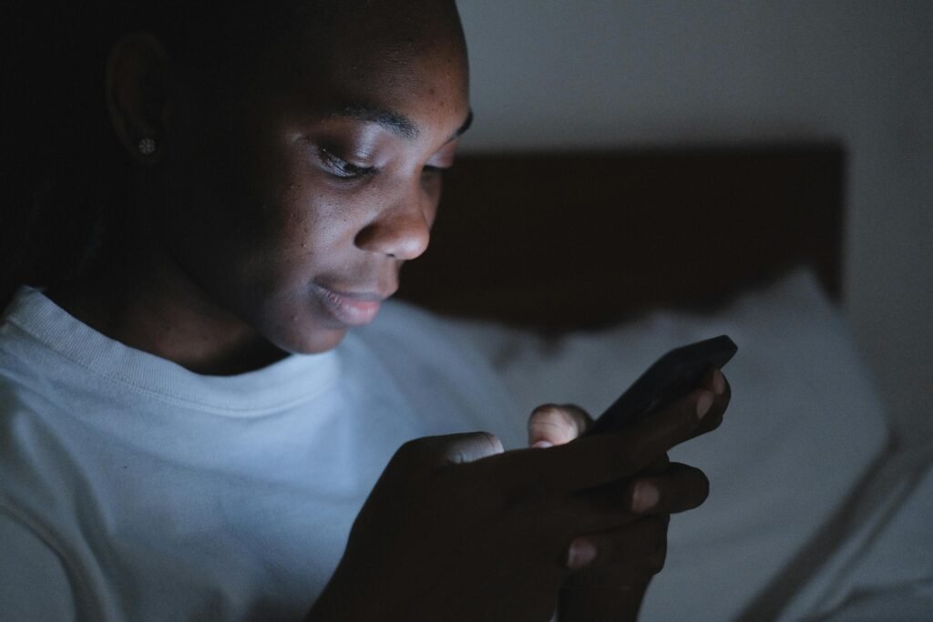 A person using a smartphone in bed at night with the screen lighting up their face