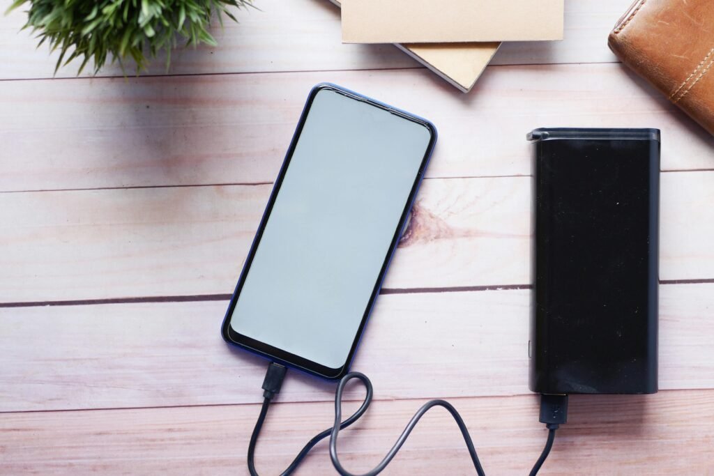 A smartphone connected to a power bank with a black cable on a wooden surface